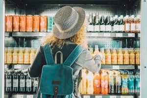 Back view of woman tourist with backpack in front of a convenience store cooler full of drinks bottles