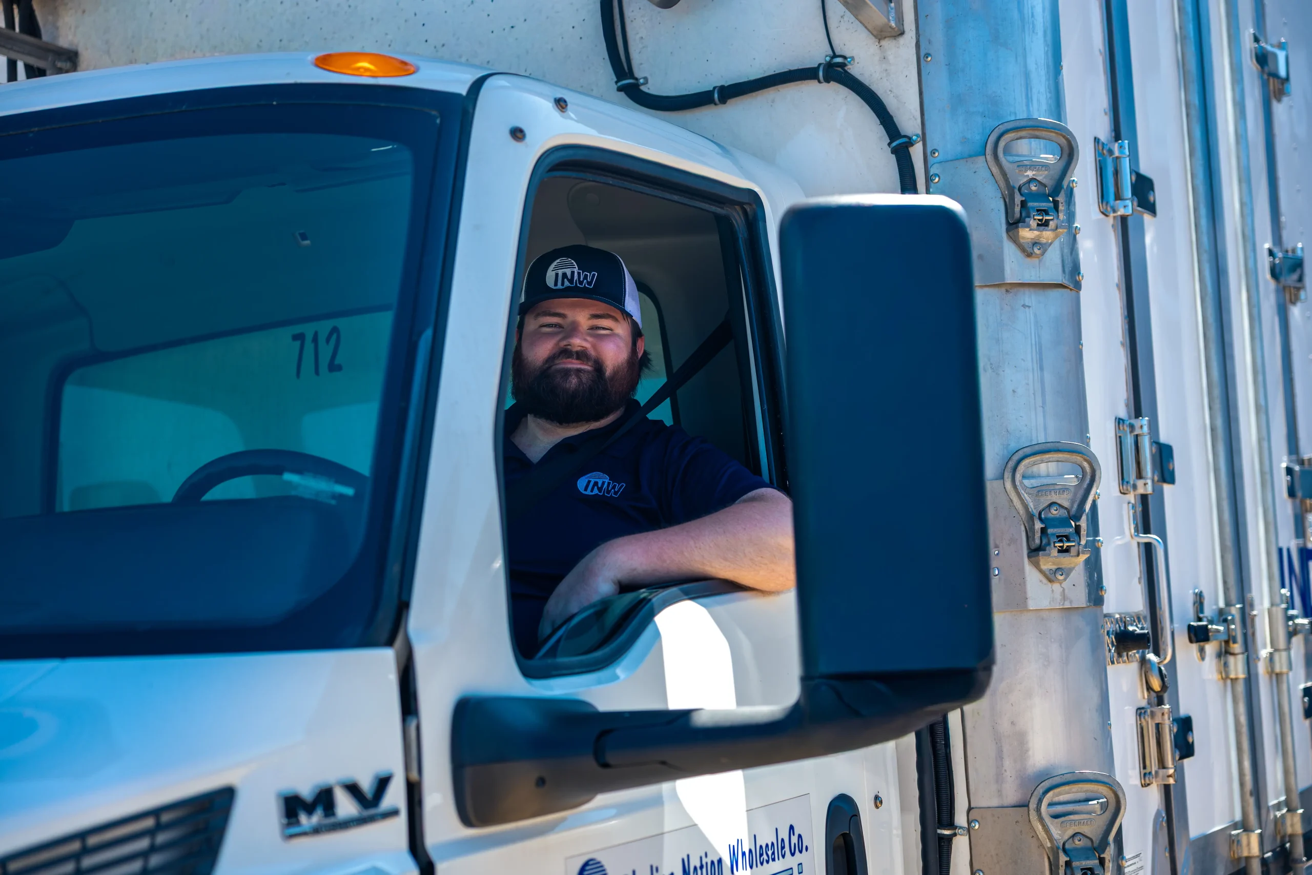 truck_recruitment_headshot_1 INW Trucker in uniform smiling and leaning out of the truck window.