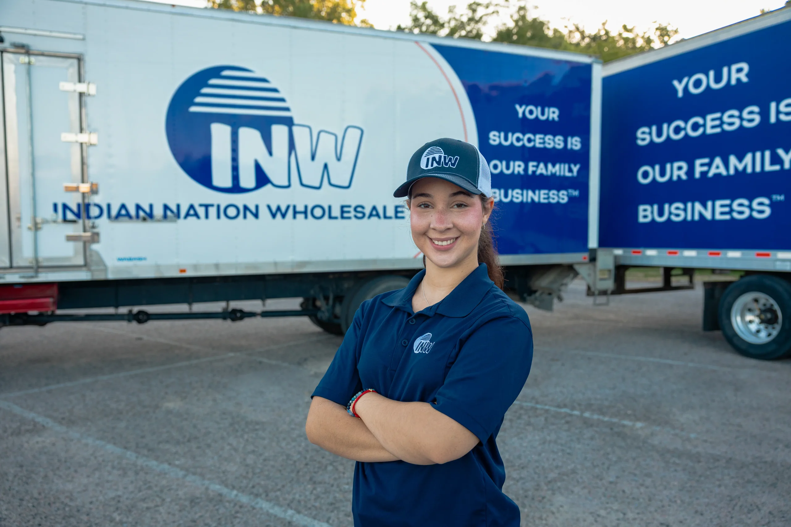 Woman in INW Trucker uniform standing in front of two INW trucks.